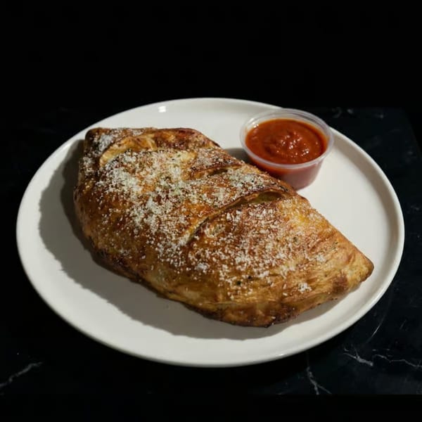 Golden-brown calzone sprinkled with parmesan cheese, served with a side of marinara sauce on a white plate.