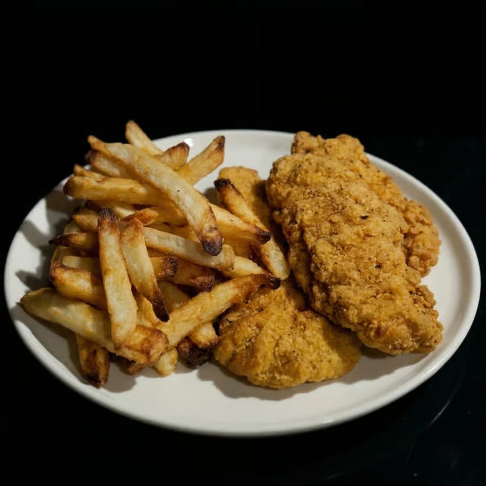 A white plate holds golden-brown french fries and crispy fried chicken tenders against a dark background.