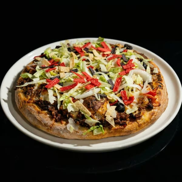 Taco pizza with ground beef, lettuce, black olives, red and white tortilla strips on a white plate.