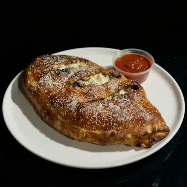 A golden-brown calzone, sprinkled with cheese, served with a side of red marinara sauce.