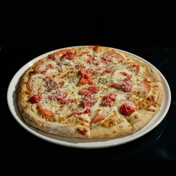 A whole pizza with white cheese, diced tomatoes, and herbs on a white plate.