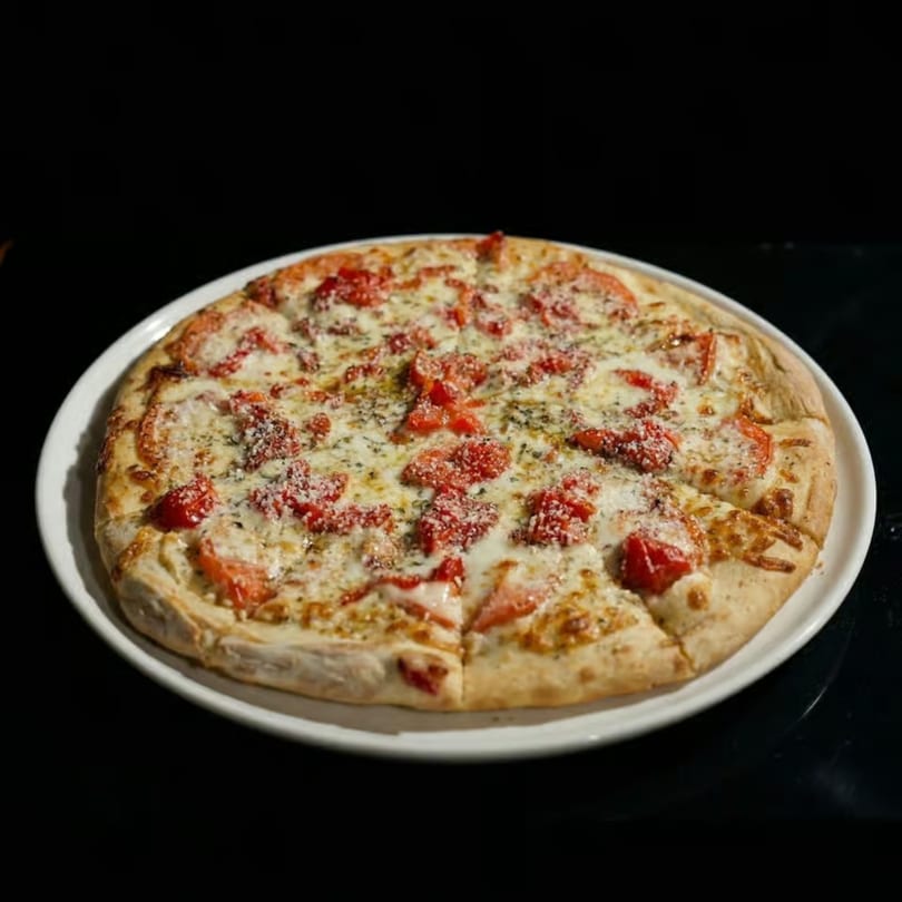 A whole pizza with white cheese, diced tomatoes, and herbs on a white plate.